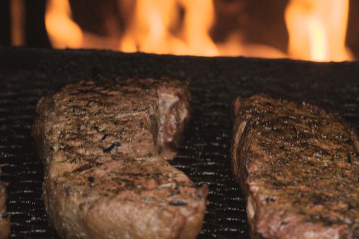 Two steaks on the grate with the fire behind them